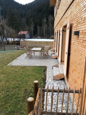 Eine einladende Terrasse vor einem Holzhaus in den Bergen, ideal für entspannte Stunden im Freien an einem klaren Tag.