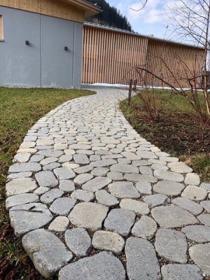 Ein geschwungener Steinweg verbindet den Garten mit einem modernen Gebäude in ruhiger Umgebung und lädt zum Spazieren ein.