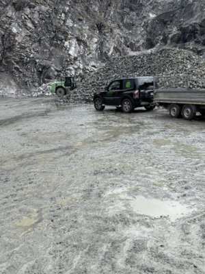 Ein Lkw und ein Bagger arbeiten in einem Steinbruch. Staub und Steine prägen die raue Landschaft des Arbeitsgeländes.