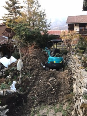 Ein kleiner Bagger arbeitet im herbstlichen Garten hinter einem Haus. Erde wird umgegraben und neue Formen entstehen.