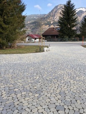 Ein gepflasterter Platz mit vielen Steinen umgeben von Bäumen und Bergen an einem klaren Tag im Frühling.