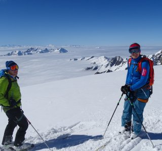 2 skifahrer, hochnebel, blauer himmel, bergpanorama