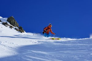 Freerider beim Skifahren im Tiefschnee auf steilem Hang, Sonnenschein, blauer Himmel, dynamische Abfahrt im alpinen Gelände.