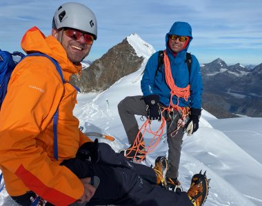 bergführer mit seilschlingen, bergsteiger mit oranger jacke, schnee, felsen