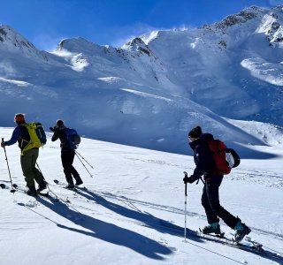 3 skitourengeher, berglandschaft, schnee, windfahnen
