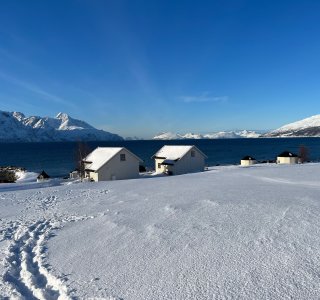 2 Häuser, fjord, schnee, blauer Himmel, berge