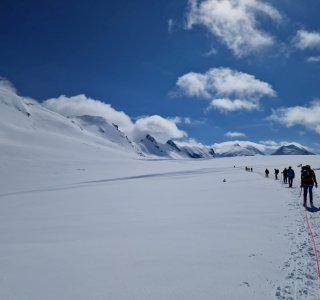 blauer himmel, wolken, schneespuren, personen am seil. gletscher