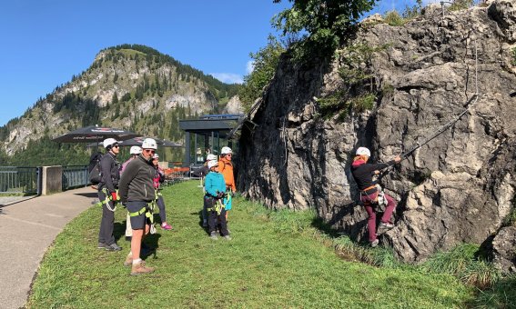 wiese, mehrere personen mit helm, klettersteig, felswand