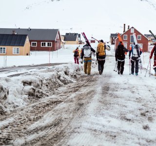 skitourengruppe zu fuss mit ski auf der schulter auf verschneiter strasse