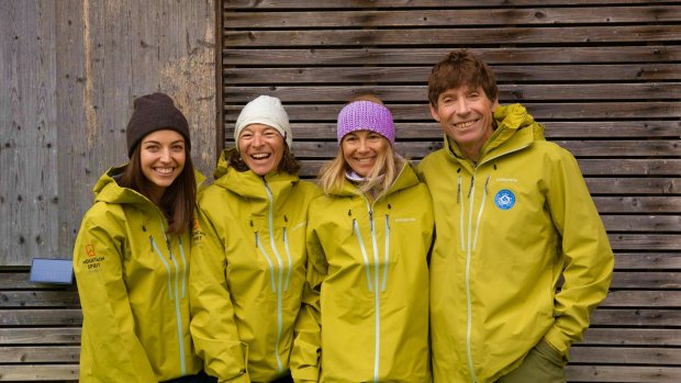 Bergschule Mountain Spirit Team Bolsterlang Mountain-Spirit-Team in grünen Outdoorjacken steht lachend vor Holzwand – Bergführer und Organisationsteam für Ski- und Abenteuerreisen.