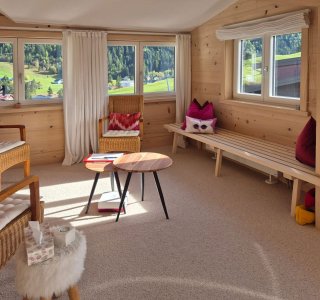 Der Raum zeigt eine helle Innenausstattung mit Blick auf die grüne Landschaft von Bergen und Wäldern.