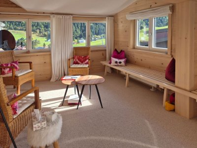 Der Raum zeigt eine helle Innenausstattung mit Blick auf die grüne Landschaft von Bergen und Wäldern.