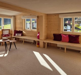 Diese gemütliche Stube hat große Fenster, helles Holz und wartet auf entspannte Stunden. Der Ausblick ins Grüne ist einladend.