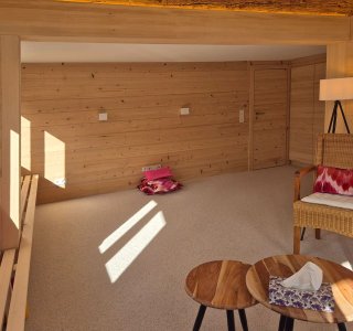 Der Raum zeigt eine gemütliche Holzverkleidung mit Lichtstrahlen, die auf dem Boden spielen und einladend wirken.