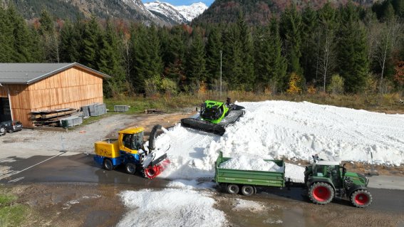 Schneeberg wird mit Traktoren abtransportiert Traktoren transportieren Schnee von einem Berg im Gebirge an einem sonnigen Tag im Herbst.