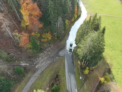 Eine Straße schlängelt sich durch den Wald und ist teilweise mit Schnee bedeckt. Es ist Herbst und die Blätter sind bunt.