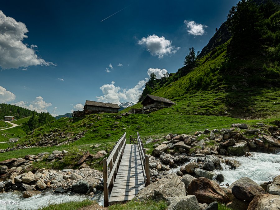 Ein Stückchen nach einer Holzbrücke liegt auf einer Anhöhe eine Südtiroler Almhütte.