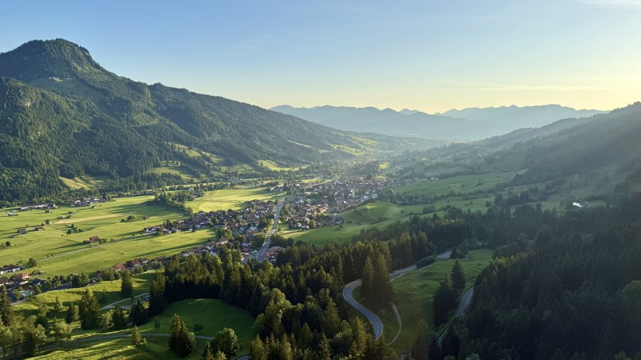 Ein Blick auf das Tal und die Berge während des Abends. Die Sonne scheint über die Landschaft und die Häuser.