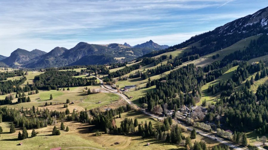 Ein Blick auf eine Berglandschaft mit Wiesen und einer Straße. Die Wiesen sind grün und erheben sich zu Bergen.
