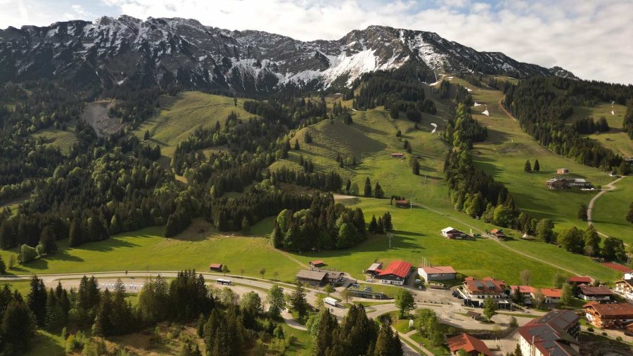 Die Landschaft zeigt grüne Wiesen, Berge und kleine Häuser in der Nähe von einem Dorf. Es ist ein sonniger Tag.