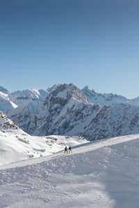 Traumkulisse mit Blick auf die Höfats Zwei kleine Personen wandern auf dem verschneiten Zeigersattel am Nebelhorn. Im Hintergrund sieht man die imposante Höfats.