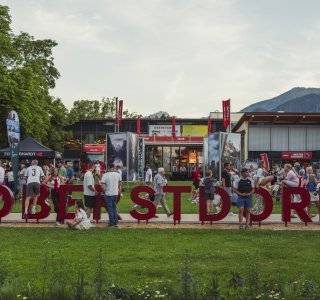 Eine Gruppe von Menschen steht vor dem Eingang einer Veranstaltung in Oberstdorf. Es ist ein schöner Tag.