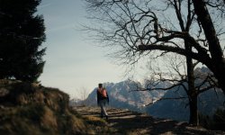 Eine Person geht einen Weg in den Bergen während des Tages. Bäume und Berge sind im Hintergrund zu sehen.