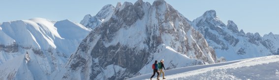 Zwei Frauen wandern an einem sonnigen Wintertag auf dem Winterwanderweg Zeigersattel am Nebelhorn. Im Hintergrund ragt die imposante Höfats empor.