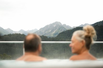 Ein Paar sitzt im Wasser und blickt auf die Berge. Die Landschaft ist grün und voller Hügel.