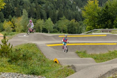 Mit dem Rad im Nordic Park Zwei Kinder fahren mit ihren Bikes auf einem BMX-Parcours in der Natur. Es ist ein sonniger Tag.
