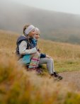 Zwei Kinder sitzen auf einer Bank und spielen in der Natur. Es ist bewölkt und die Umgebung ist grün.