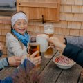 Eine Familie genießt Getränke und Snacks in einer Berghütte. Es ist eine fröhliche Atmosphäre beim gemeinsamen Essen.