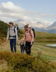 Eine Familie geht auf einem Wanderweg in den Bergen. Es ist tagsüber und die Landschaft ist grün.