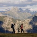 Eine Familie geht mit einem Kind in den Bergen bei den Alpen. Die Sonne scheint und die Sicht ist klar.