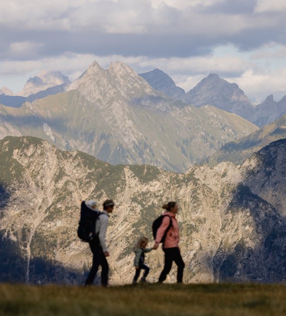 Eine Familie geht mit einem Kind in den Bergen bei den Alpen. Die Sonne scheint und die Sicht ist klar.