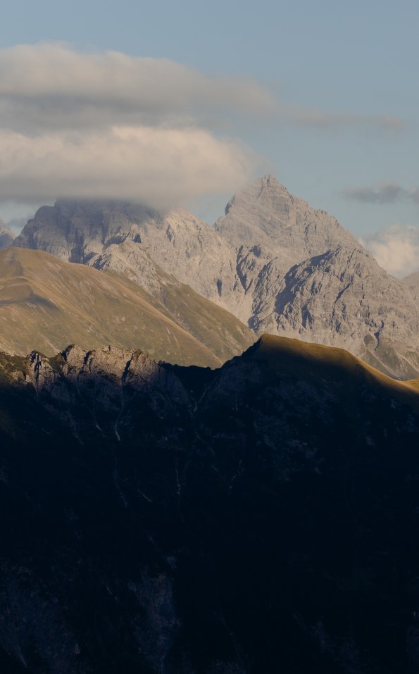 Berge stehen vor einem klaren Himmel. Die Sonne geht hinter den Gipfeln unter. Schatten fallen über das Tal.