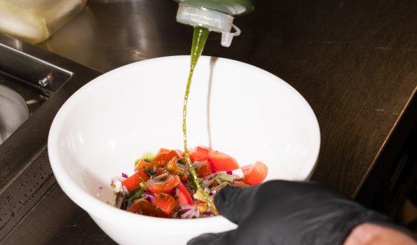 Jemand fügt Dressing auf einen Salat in einer modernen Küche hinzu. Es werden frische Zutaten verwendet.