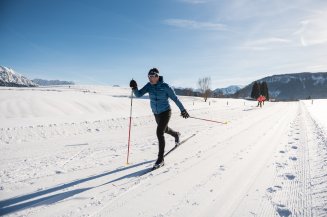 Ein Langläufer gleitet bei sonnigem Winterwetter über eine präparierte Loipe in Bolsterlang.
