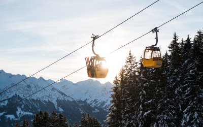 Gondeln der Hörnerbahn vor Bergkulisse und Wintersonne. Gondeln der Hörnerbahn fahren im Gegenlicht über verschneite Bäume und die Allgäuer Bergwelt.