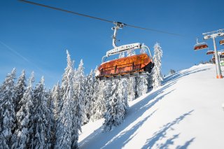 Ein orangefarbener Sessellift fährt durch die verschneite Winterlandschaft im Skigebiet Bolsterlang.