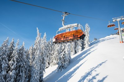 Ein orangefarbener Sessellift fährt durch die verschneite Winterlandschaft im Skigebiet Bolsterlang.