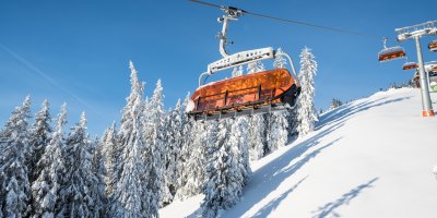 Ein orangefarbener Sessellift fährt durch die verschneite Winterlandschaft im Skigebiet Bolsterlang.
