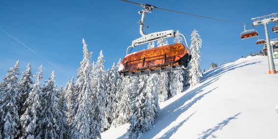 Orangefarbener Sessellift im verschneiten Skigebiet Bolsterlang. Ein orangefarbener Sessellift fährt durch die verschneite Winterlandschaft im Skigebiet Bolsterlang.