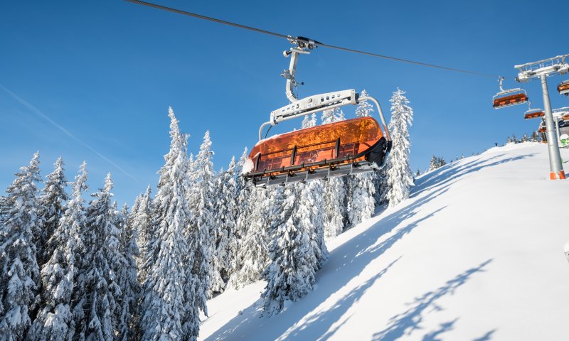 Ein orangefarbener Sessellift fährt durch die verschneite Winterlandschaft im Skigebiet Bolsterlang.