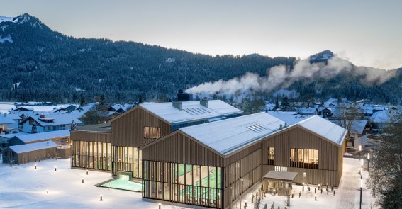 Außenansicht der Therme Oberstdorf im Winter mitten in den Allgäuer Bergen mit Blick auf die Becken Mitten im Schnee bietet die Therme Oberstdorf im Allgäu die perfekte Umgebung zum Entspannen und Aufwärmen an einem kalten Wintertag.