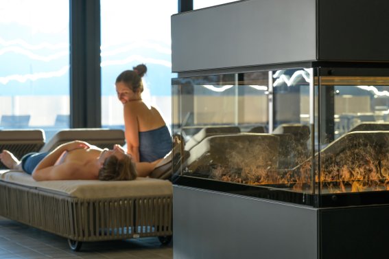 Zwei Saunagäste entspannen im Kaminzimmer der Therme Oberstdorf in den Allgäuer Bergen mit Feuerprasseln Das Kaminzimmer bietet allen Saungästen pure Entspannung zwischen den Saunagängen in der Therme Oberstdorf.