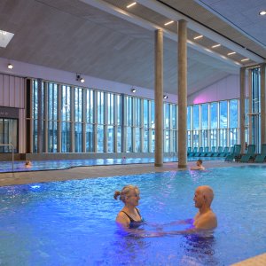 Badegäste im Erlebnisbecken in der Therme Oberstdorf mit integriertem Wasserfall und Massagedüsen Das Erlebnisbecken in der Therme Oberstdorf bietet Entspannung durch Massagedüsen und einen barrierefreien Zugang.