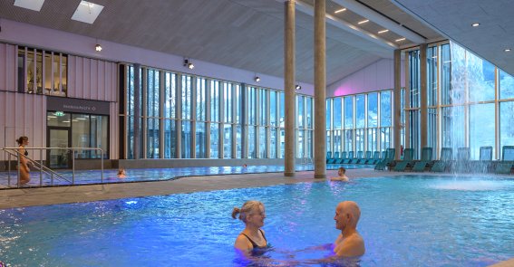 Badegäste im Erlebnisbecken in der Therme Oberstdorf mit integriertem Wasserfall und Massagedüsen Das Erlebnisbecken in der Therme Oberstdorf bietet Entspannung durch Massagedüsen und einen barrierefreien Zugang.