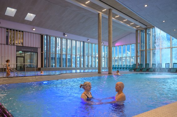 Bathers in the adventure pool at the Oberstdorf thermal baths with integrated waterfall and massage jets The adventure pool at the Oberstdorf thermal baths offers relaxation through massage jets and barrier-free access.
