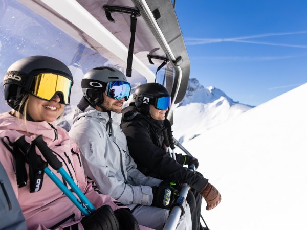 Drei Skifahrer fahren gemeinsam mit dem Sessellift bergauf und blicken voller Vorfreude auf den nächsten Run.